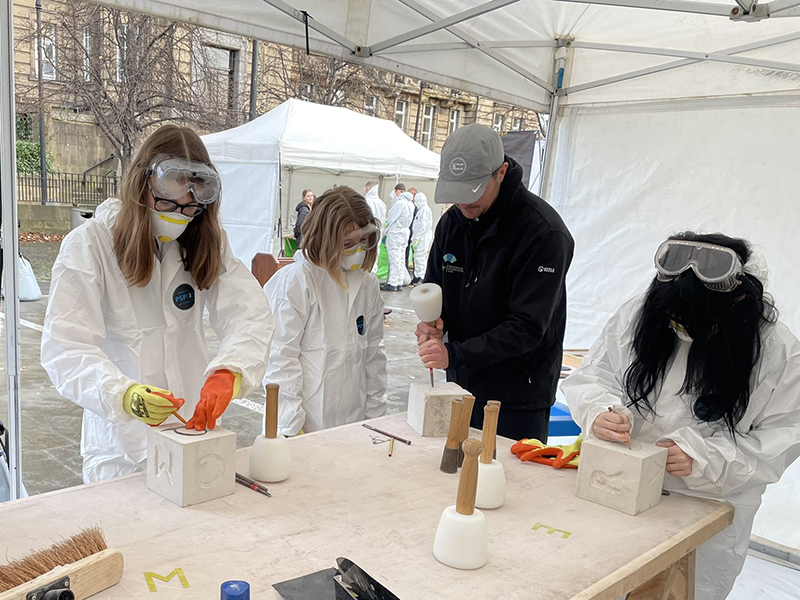 A group of young people try out stone carving in a white marquee as part of the COP26 Build Your Future traditional skills demonstrations.