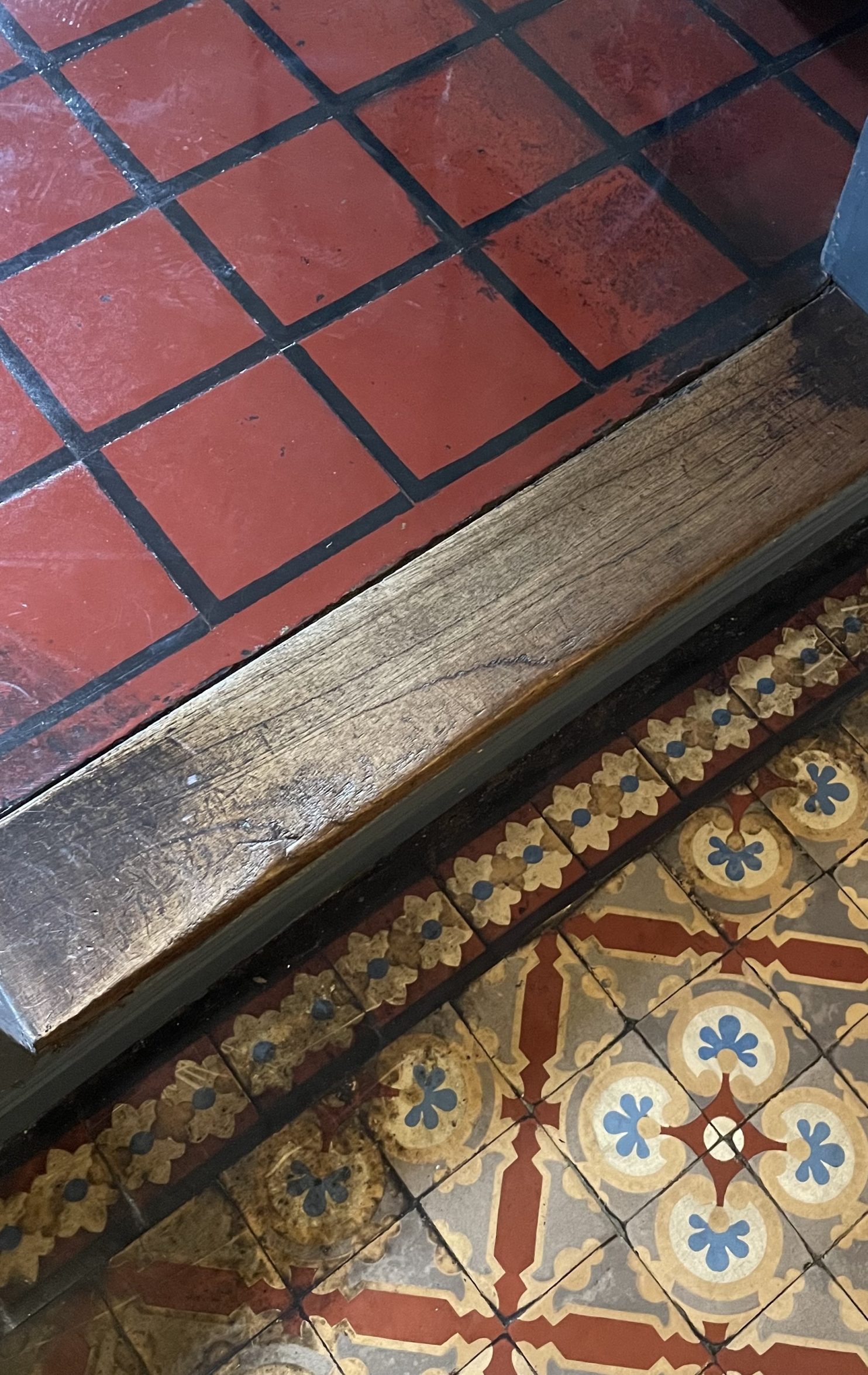 A threshold between two tiled floors; one ornate and one plain.